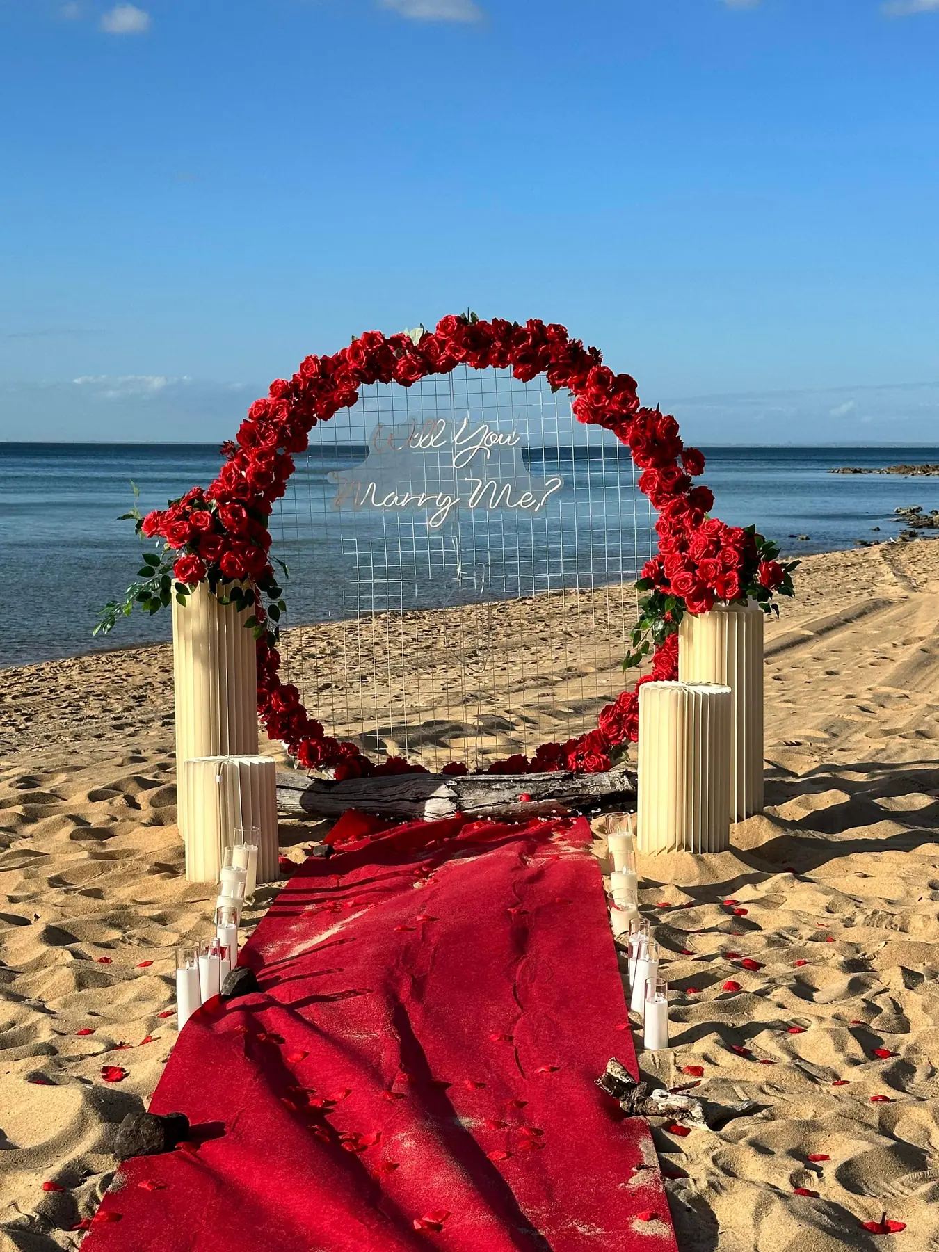 Rose ring arch and red carpet on the sand at a Port Phillip Bay beach on a clear morning