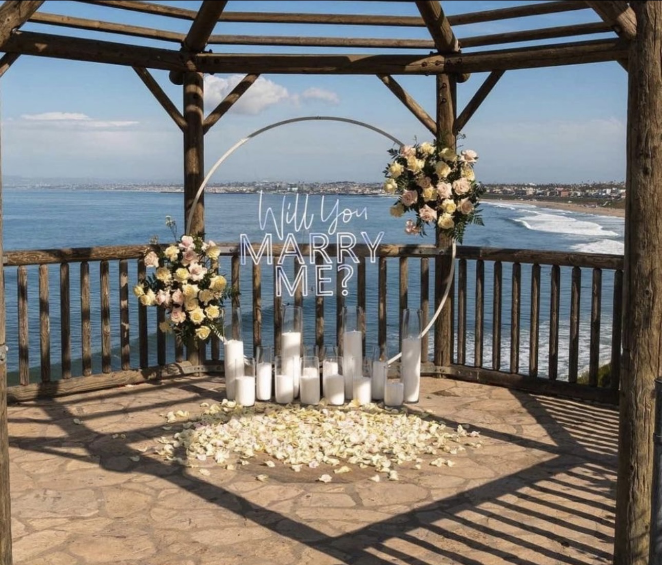 Light-up MARRY ME marquee letters beside a bouquet of pink roses on a table