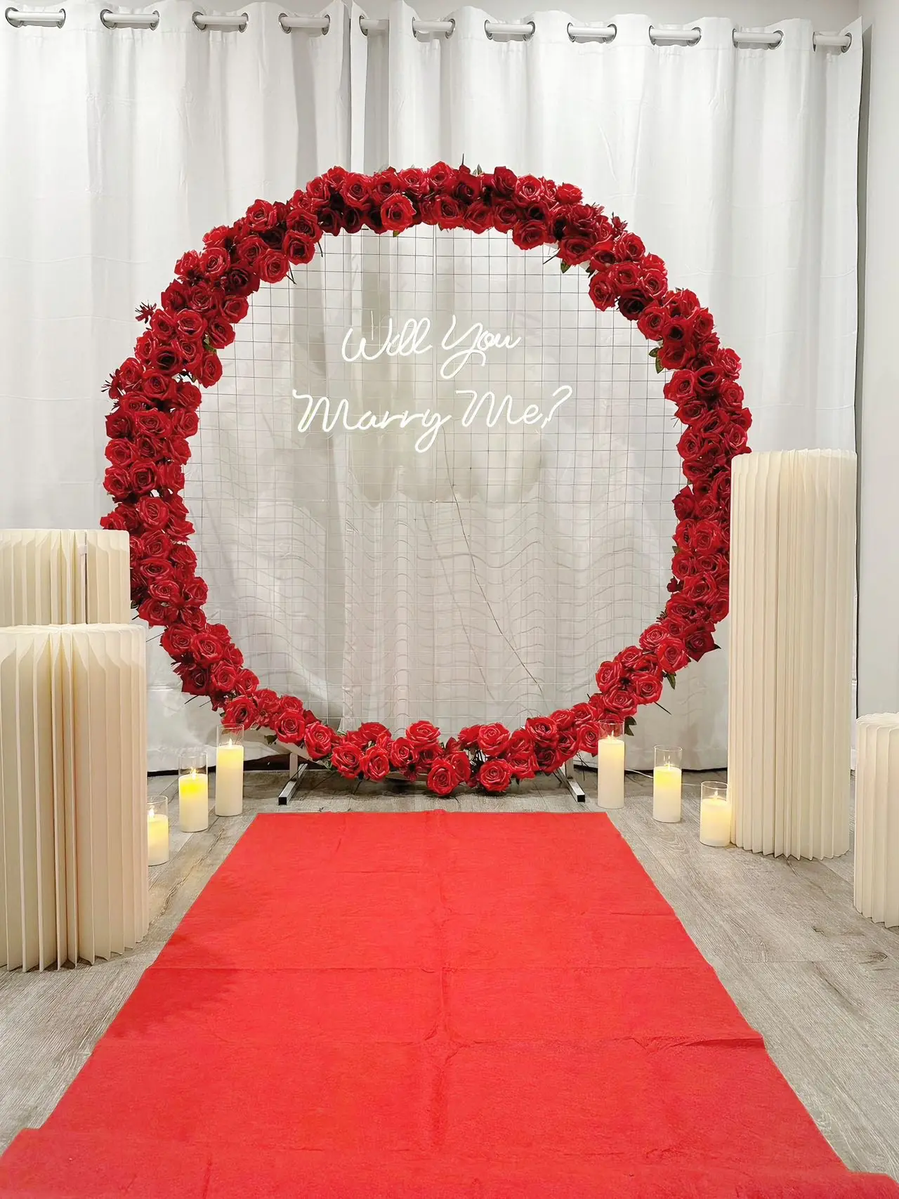 Rose ring arch, roman pillars, candles and red carpet arranged indoors against a white curtain